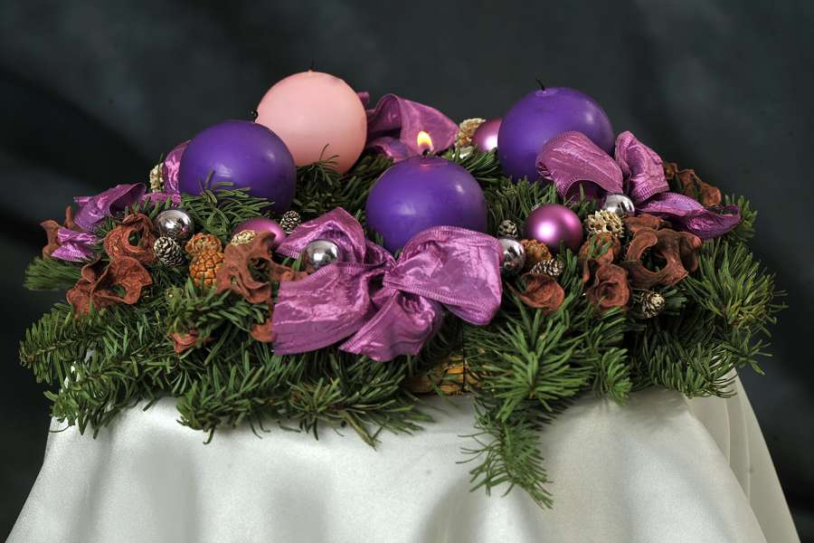 An Advent wreath with three violet candles and one rose candle, the first violet candle lit for the first Sunday of Advent
