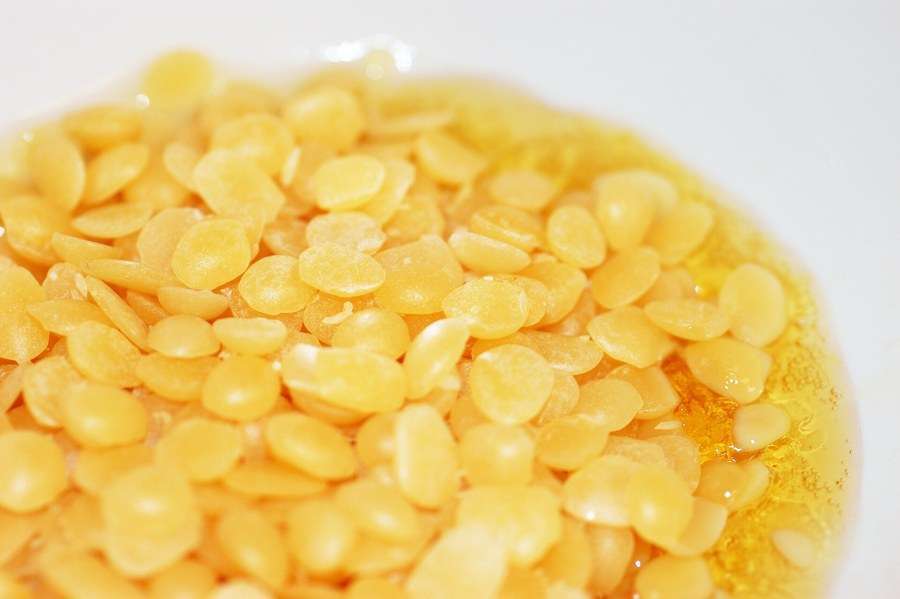 Golden beeswax pellets melting in a white bowl