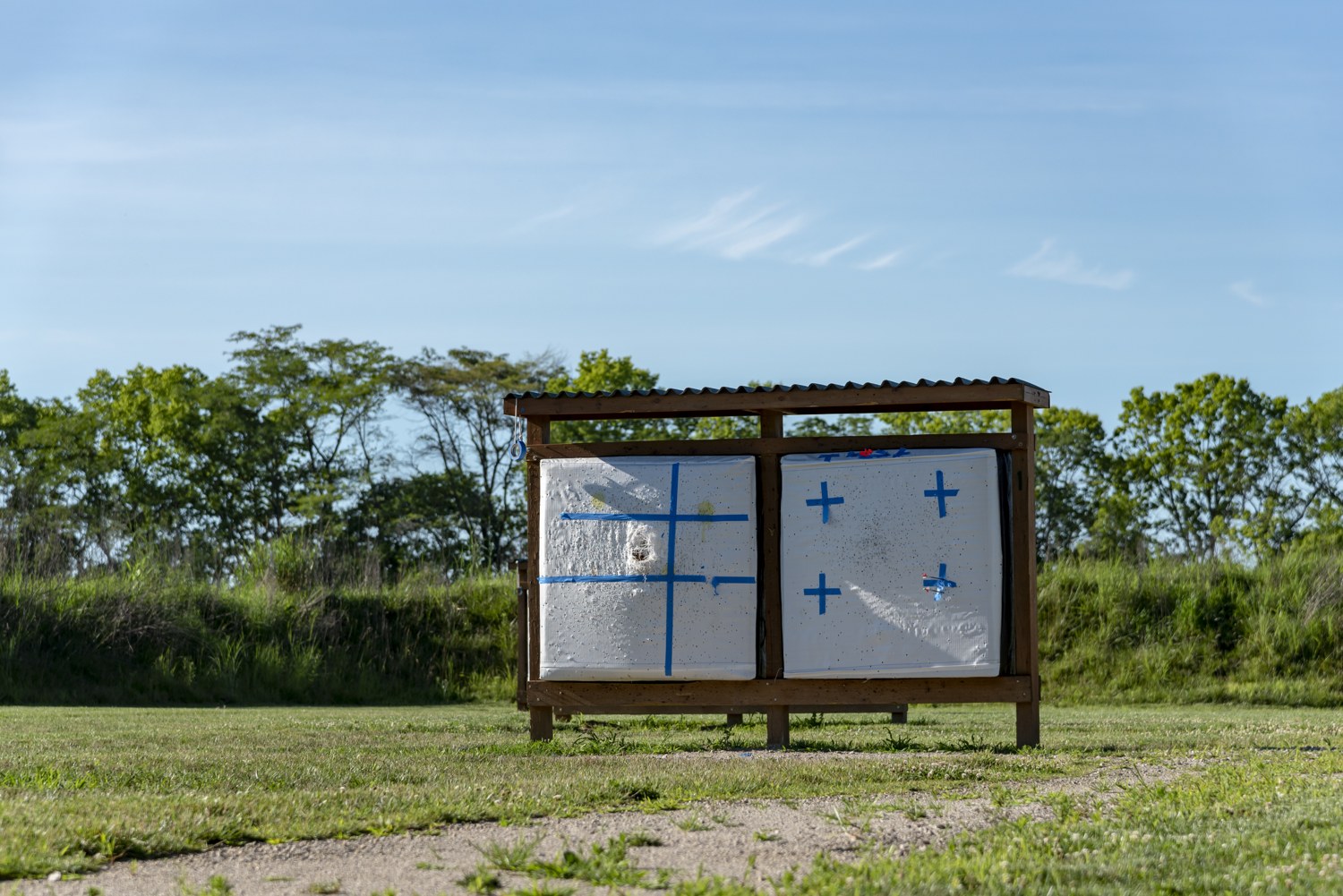 Two pale rectangular archery targets with blue markings in a roofed wooden frame outdoors
