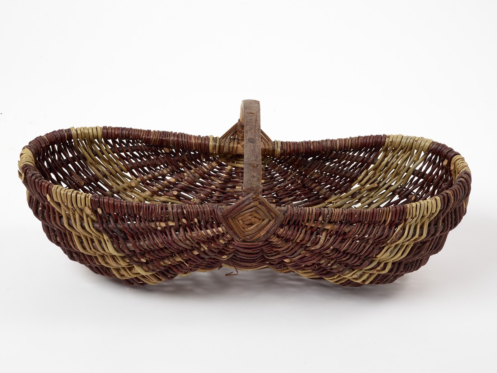 An elongated woven basket with a central handle and alternating pale and dark bands