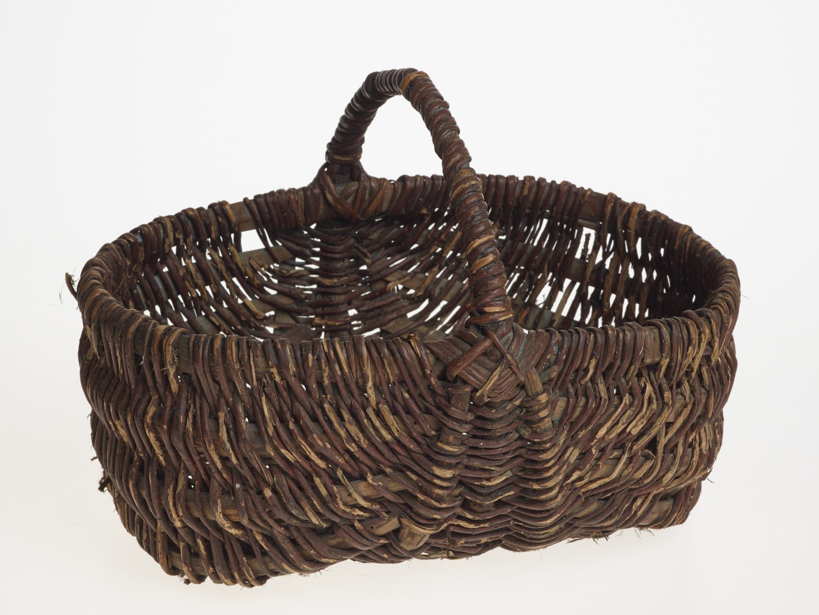 A dark woven basket with a curved handle on a white background