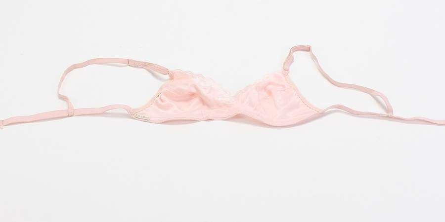 A pale pink bra laid flat on a white studio background