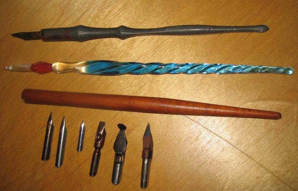 Three dip-pen holders and six separate nibs laid out on a wooden surface in December 2004