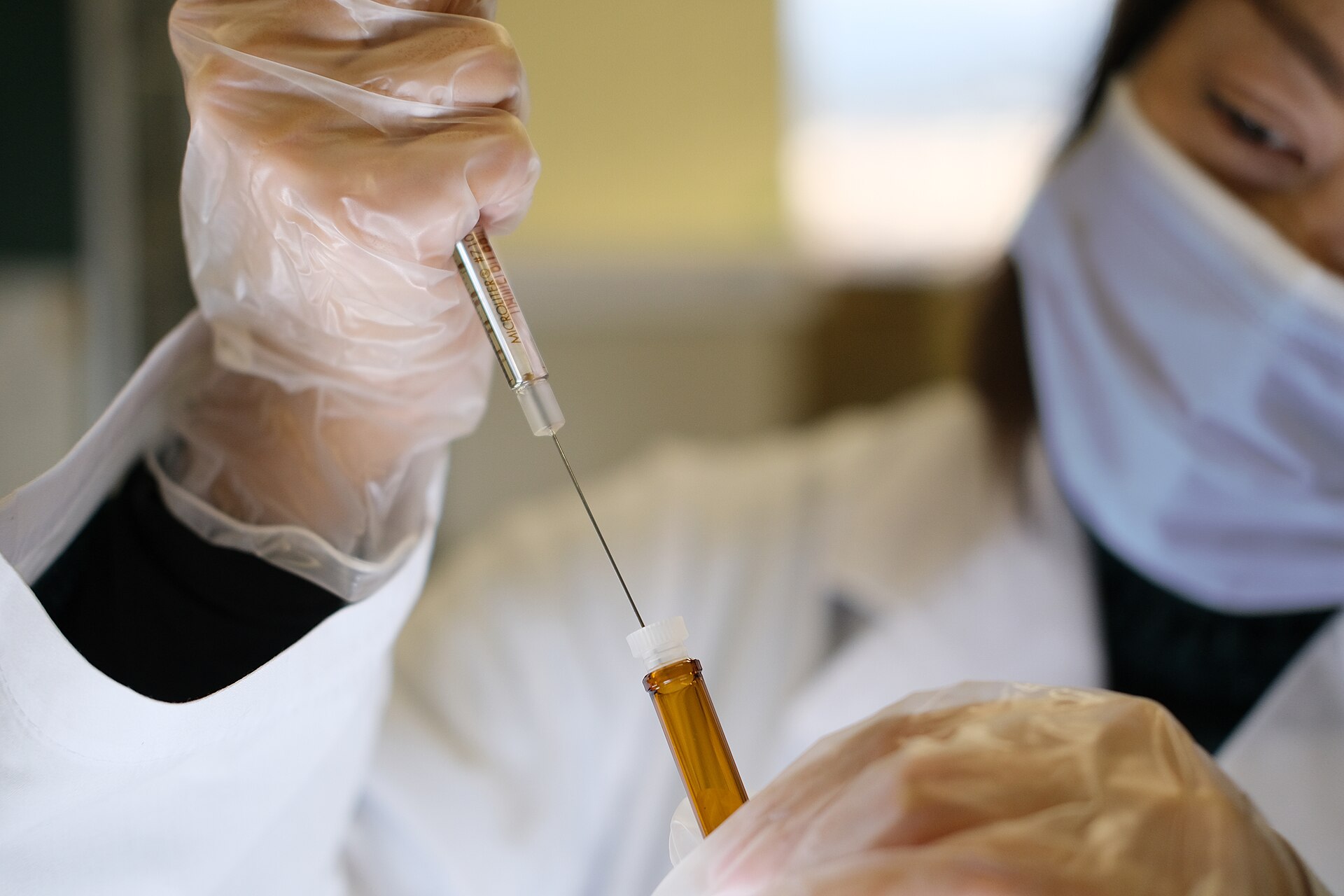Gloved hands drawing a vaccine dose from a vial into a syringe