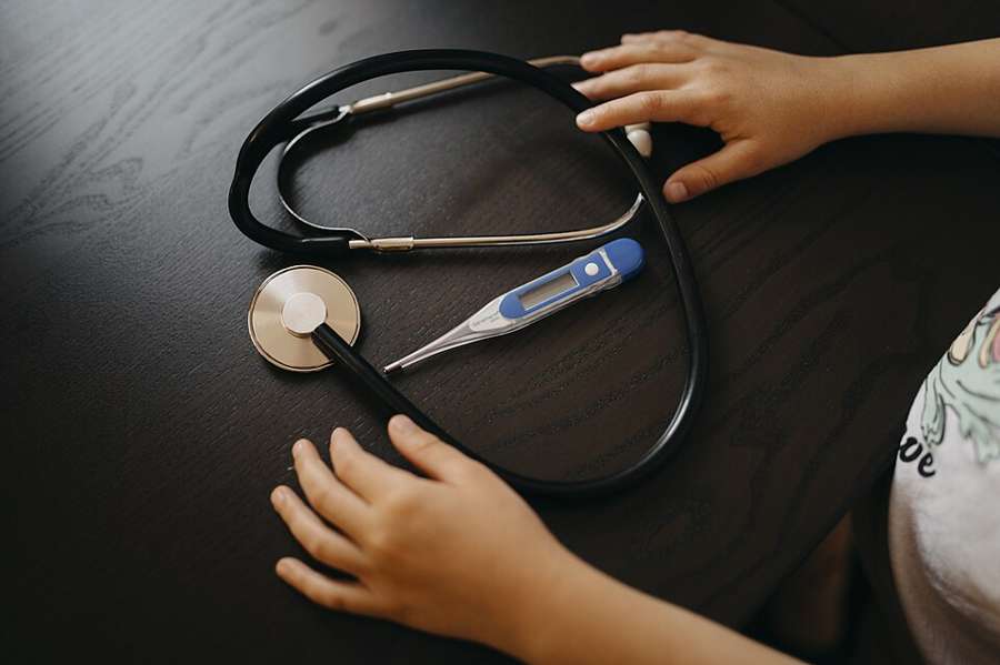 A child's hands reach for a stethoscope and thermometer on a table