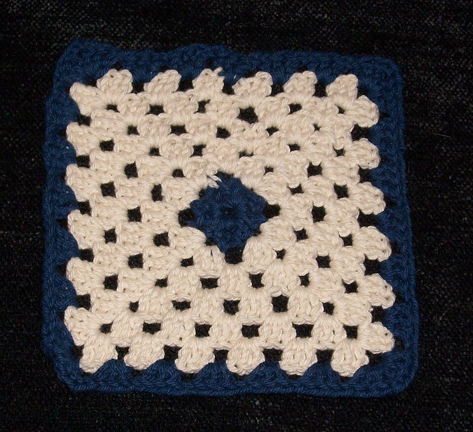 A cream crochet granny square with a dark blue centre and border on a dark background