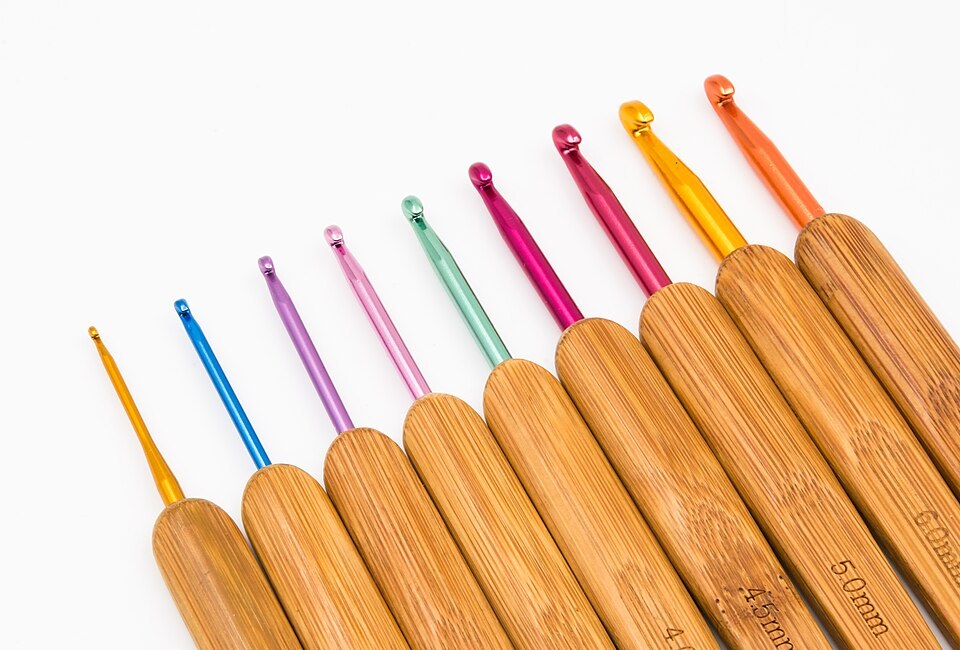 A diagonal row of colourful metal crochet hooks with wooden handles on a white background