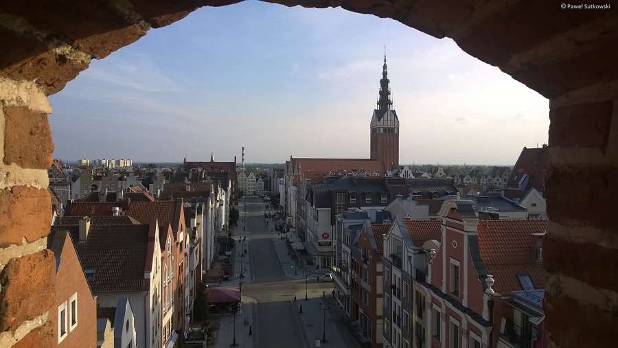 Rebuilt tenement facades along an old-town street in Elbląg, with the tower of St Nicholas Cathedral behind