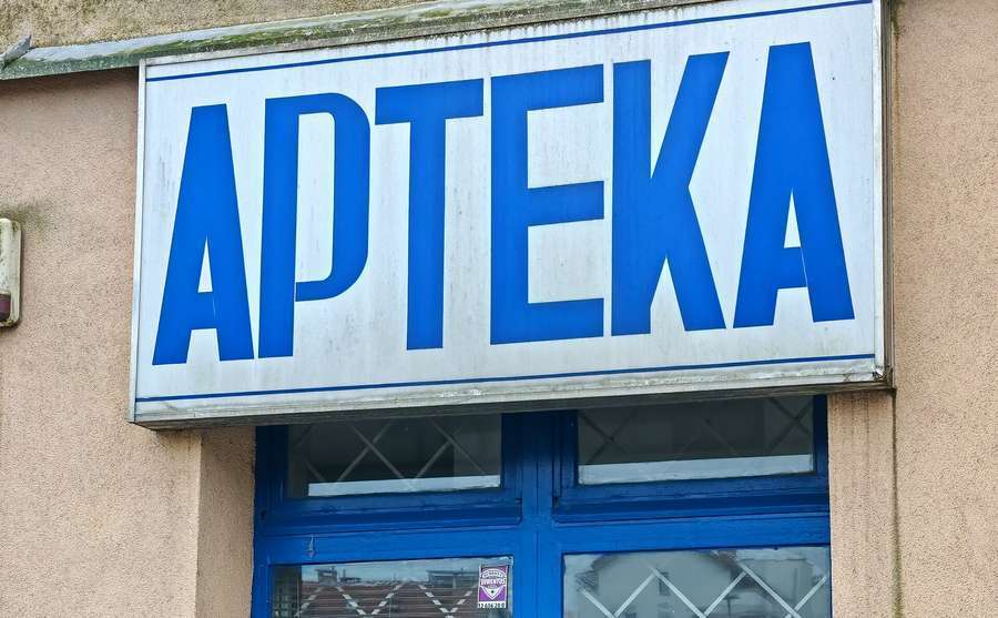 A blue and white APTEKA pharmacy sign above a shop entrance in Krakow, Poland