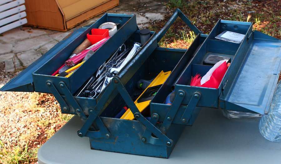 An open metal toolbox filled with wrenches, a drill and hand tools
