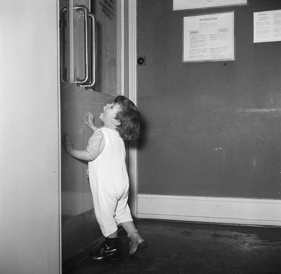 Toddler in overalls by a door