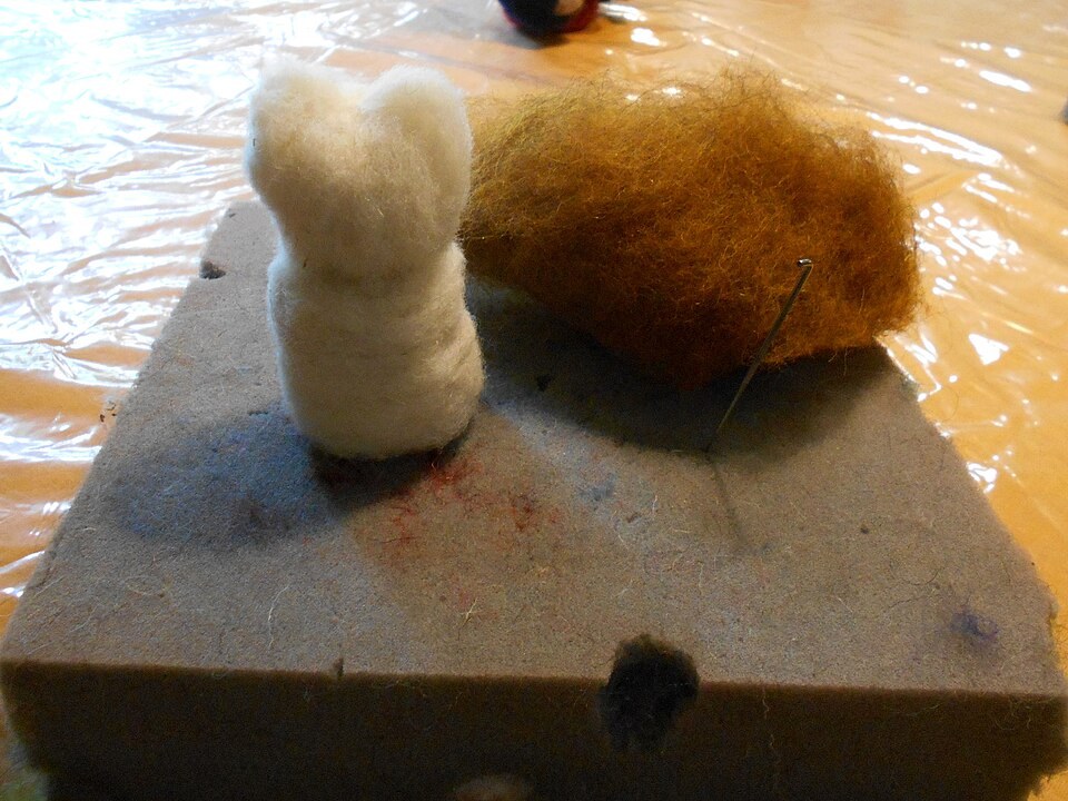 Needle-felting support with a shaped wool figure, loose wool and a specialist needle