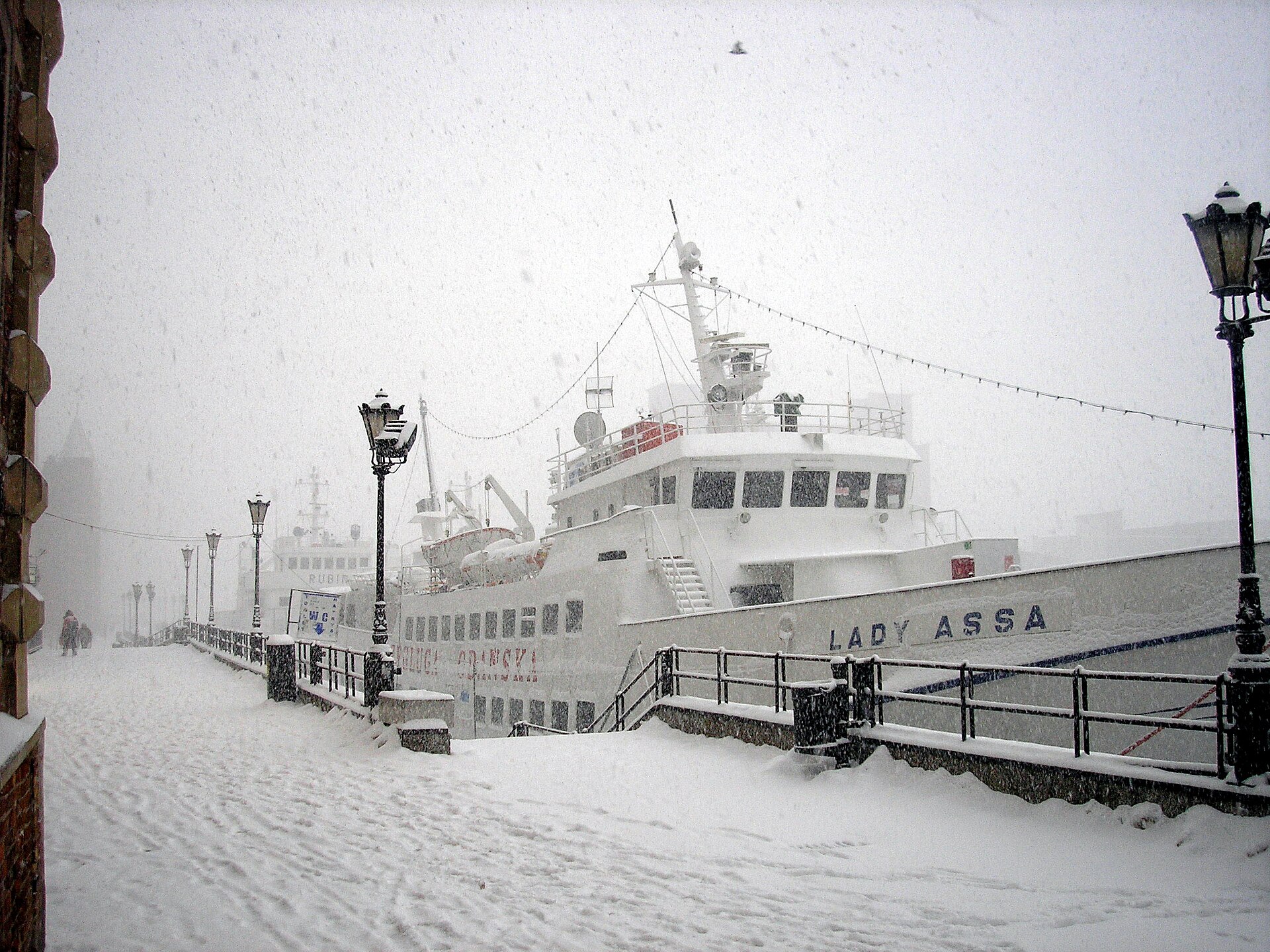 A ship moored along the snowy Długie Pobrzeże embankment on the Motława river in Gdańsk during heavy snowfall
