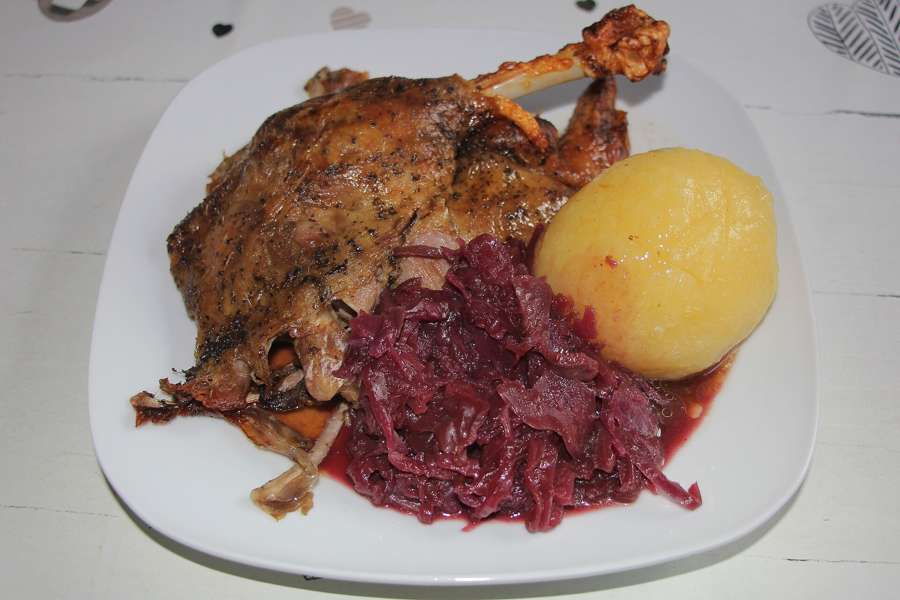 Roast goose leg with red cabbage and a potato dumpling on a white plate