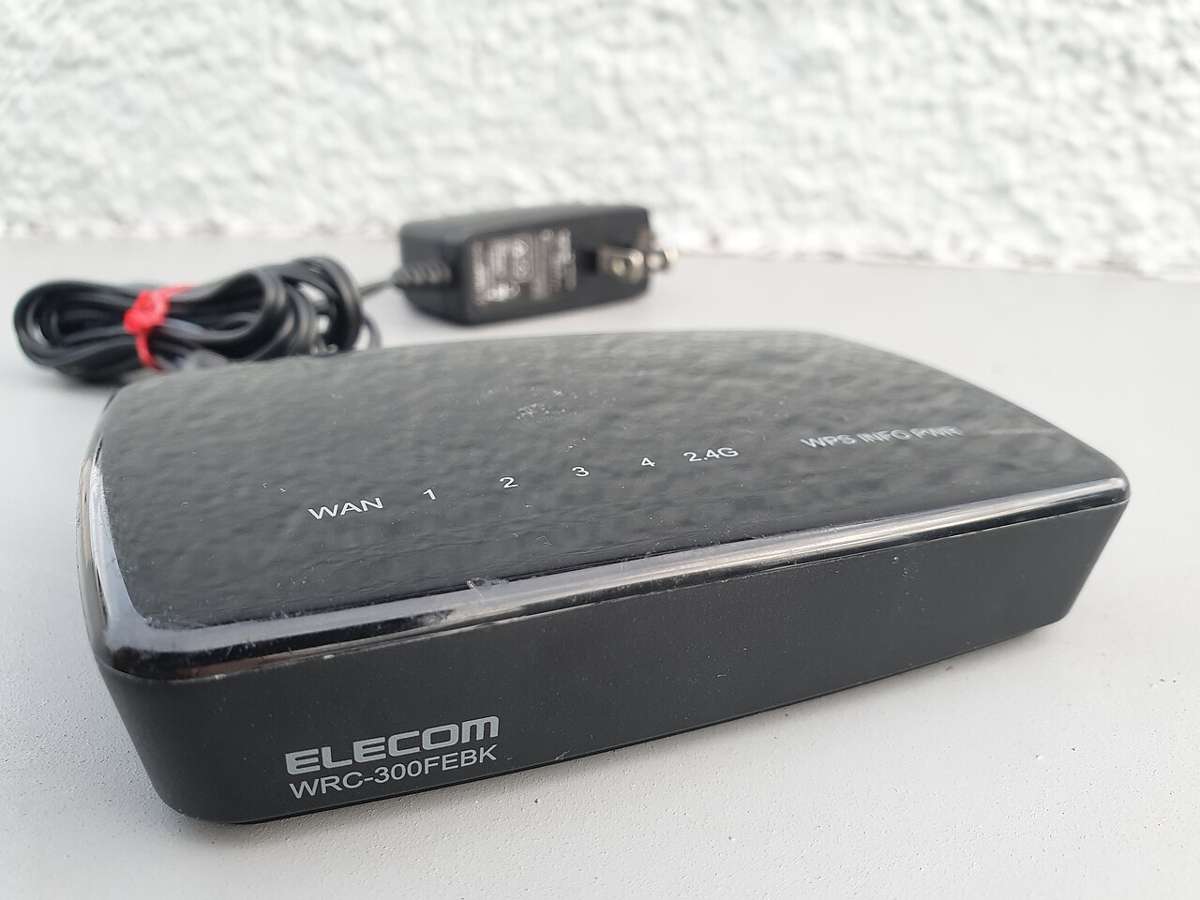 Black Wi-Fi router with power adapter on a grey surface