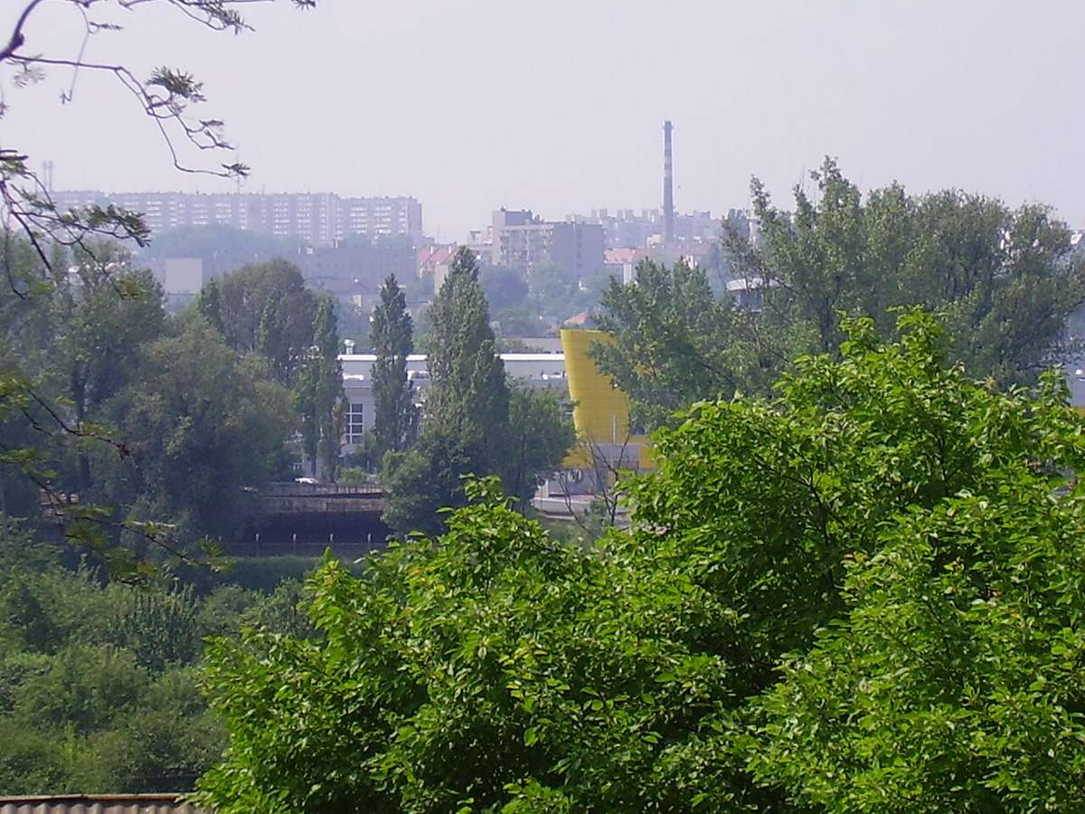 View over trees towards buildings and a chimney in Kalisz