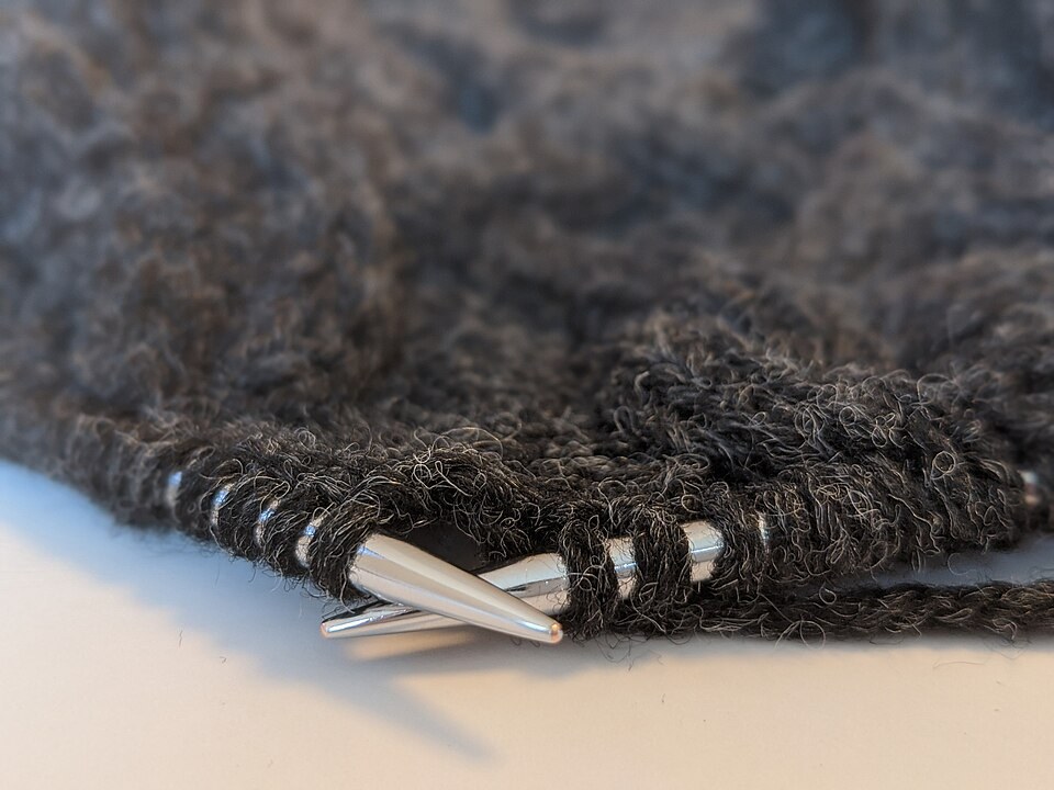 Metal knitting needles holding stitches in a dark knitted fabric