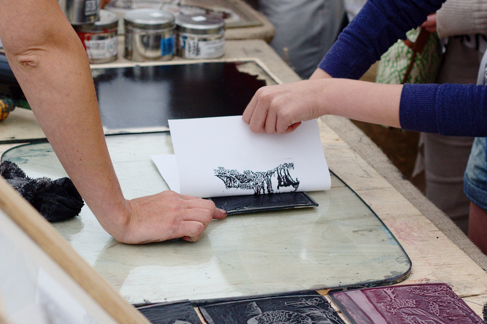 A paper sheet being lifted from a linocut block to reveal a black print in August 2013