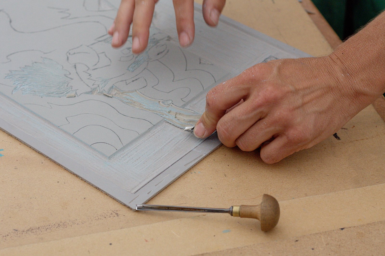 Hands carving a design into a linoleum block with a handheld tool in August 2013