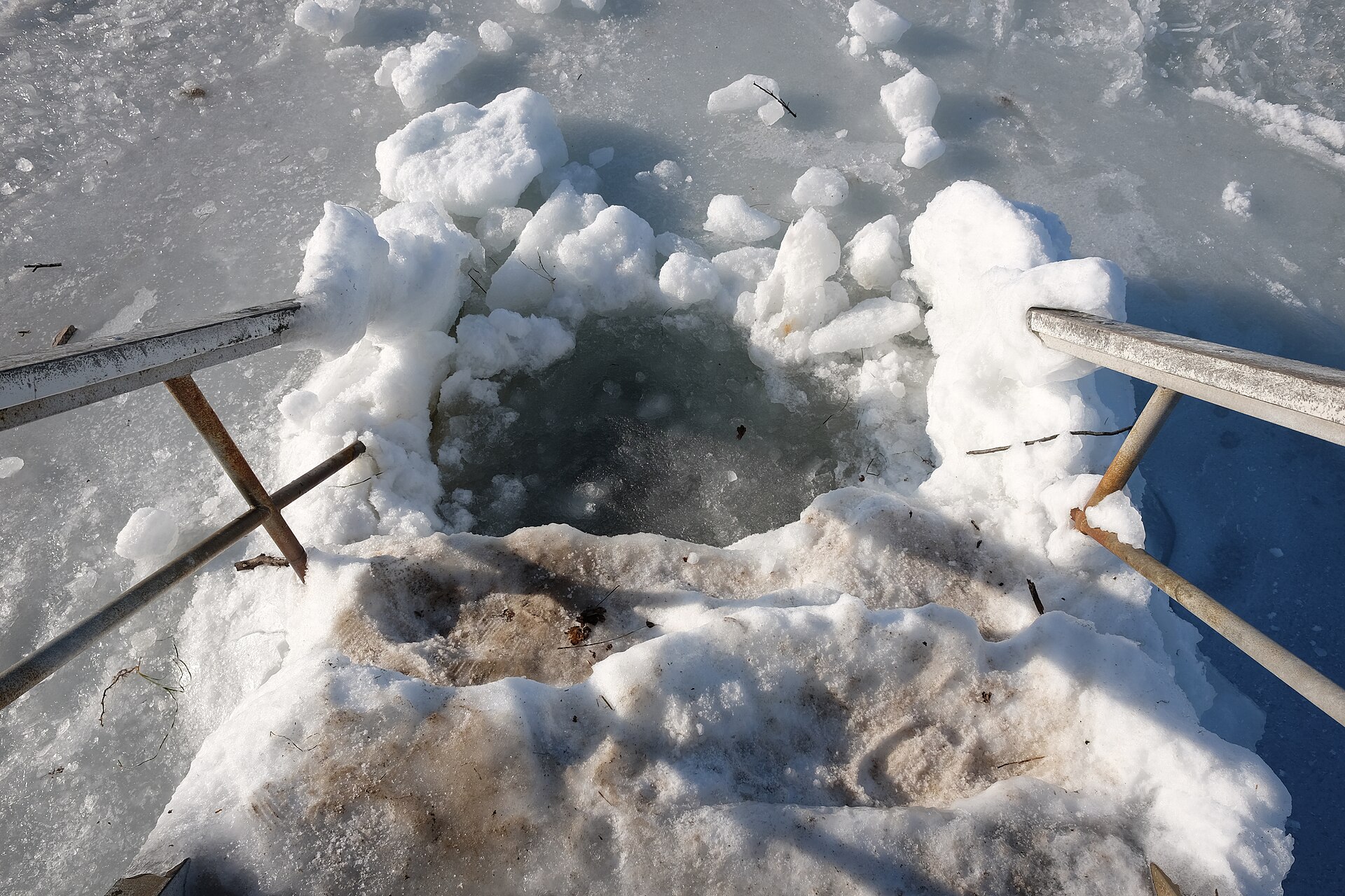 A metal ladder descending into a dark ice hole cut in a frozen sea