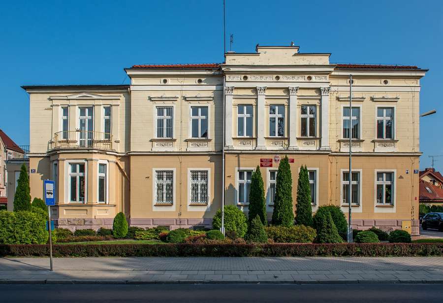 Historic municipal office building in Oleśnica with trimmed hedges