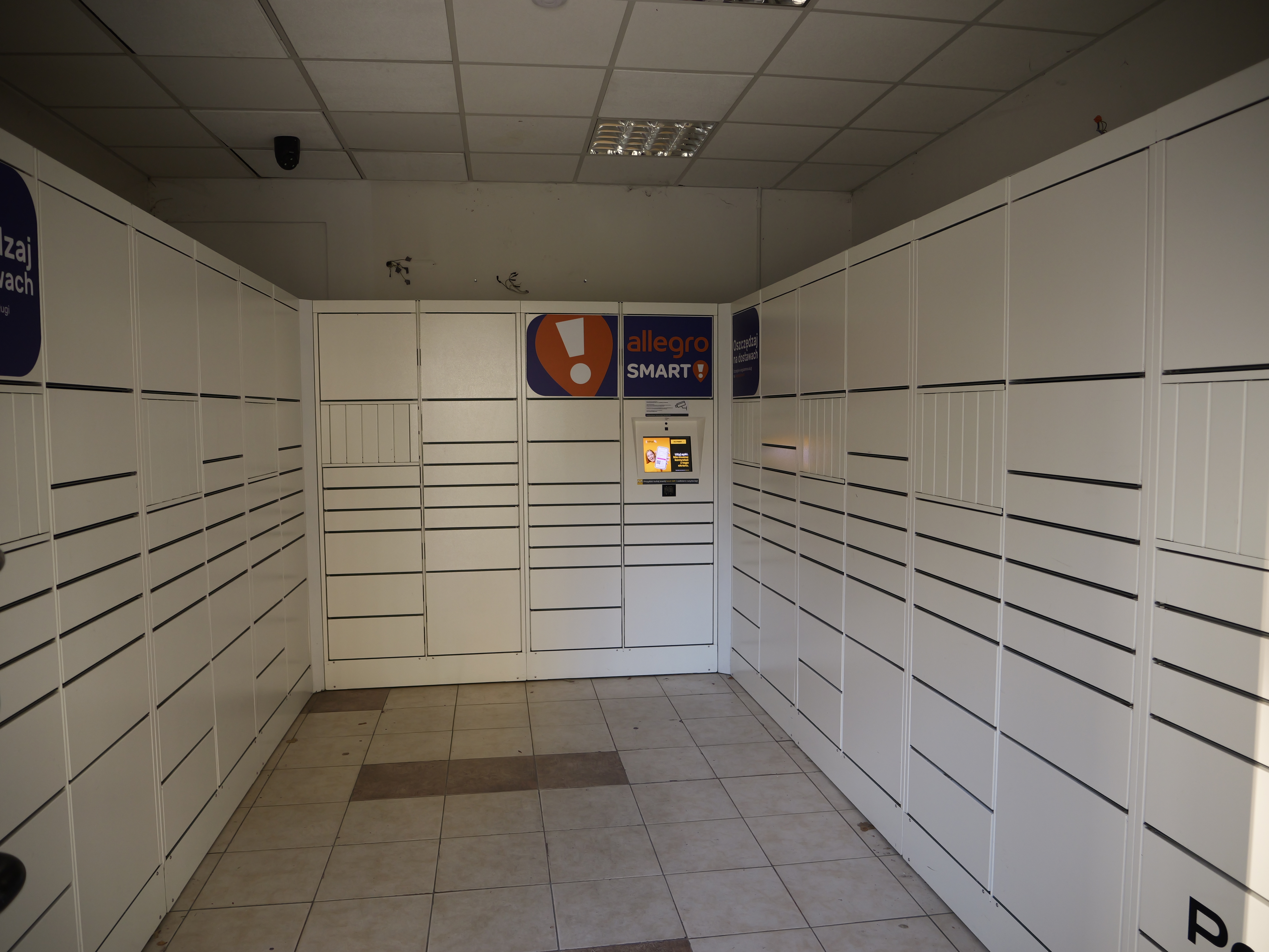 Inside a paczkomat room: rows of InPost lockers with a collection screen and Allegro Smart branding