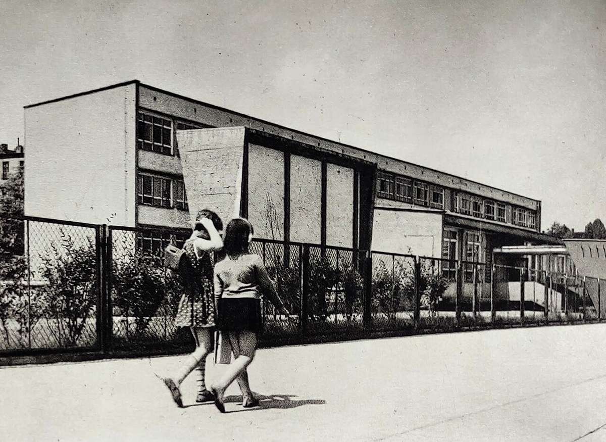A school building with two girls walking by the fence