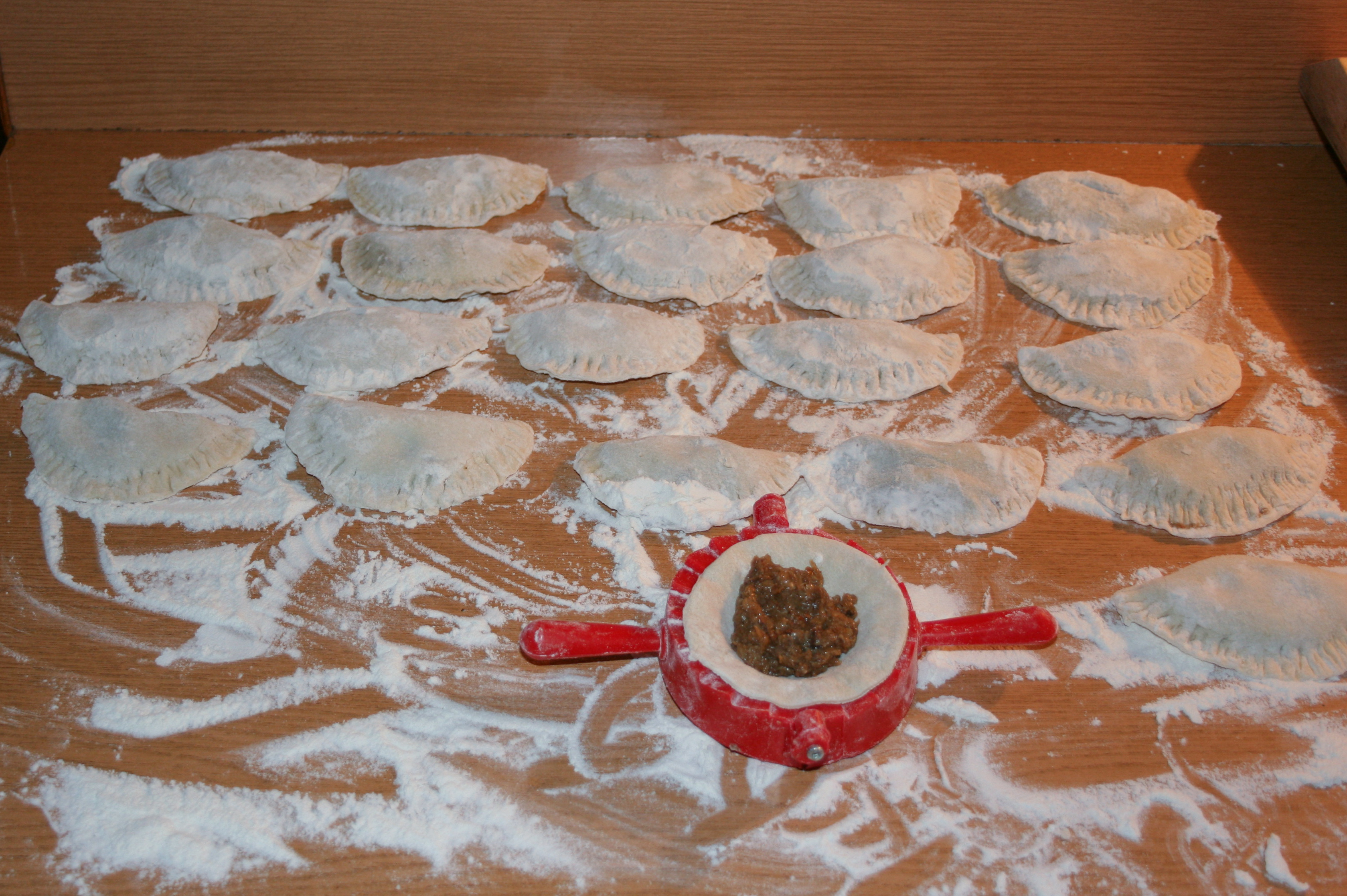Pierogi being sealed on a floured board in Gniezno, with a pierogi press holding one dumpling in progress