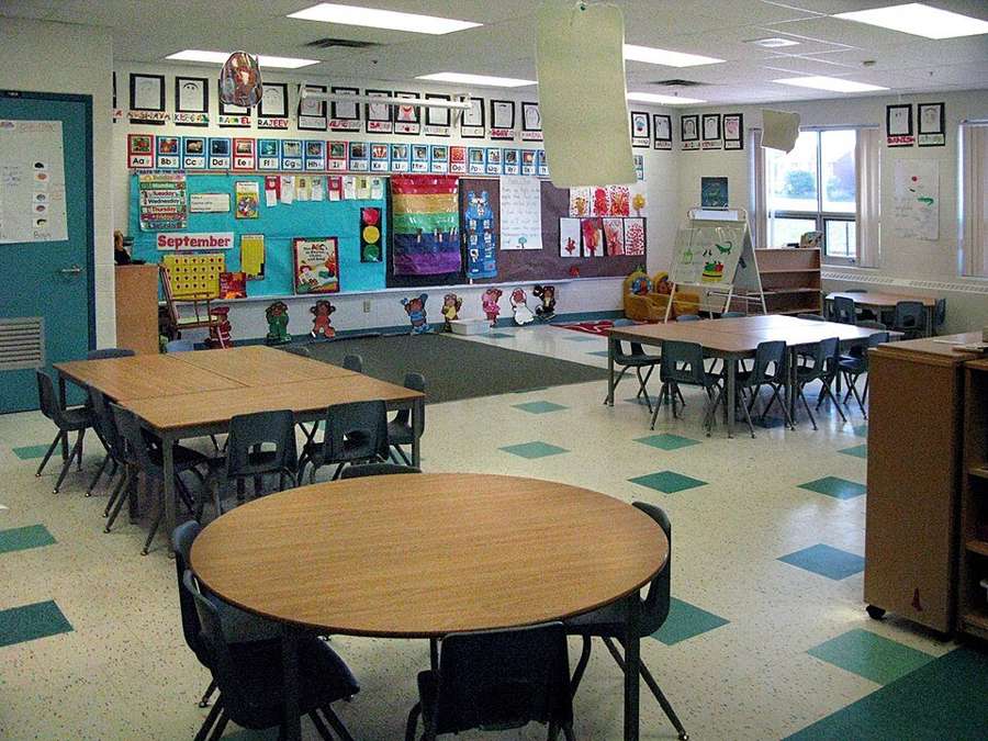 A bright, empty kindergarten classroom with small tables and chairs