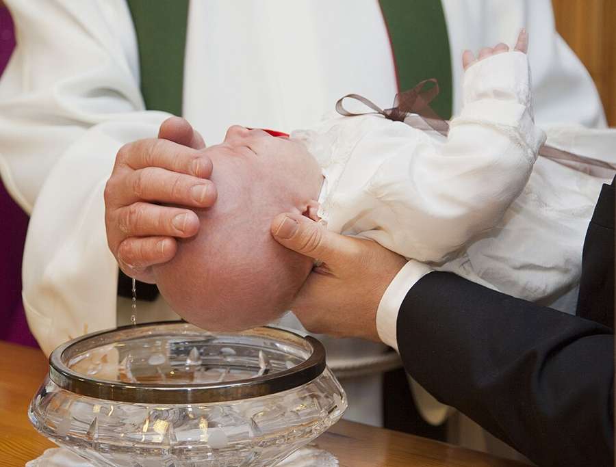 An infant in a white christening gown being baptized at the font