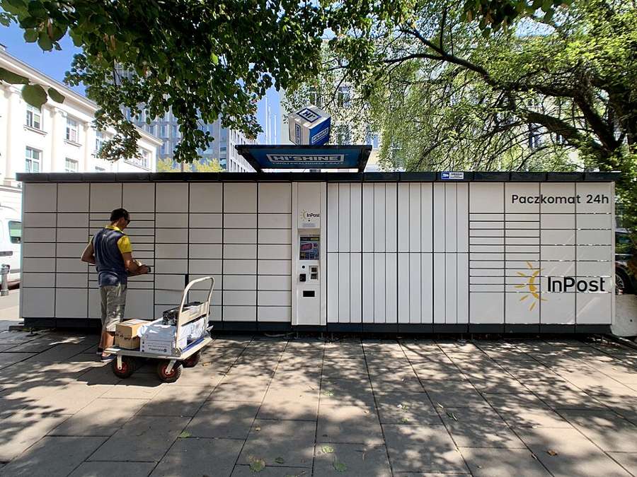 A courier loading parcels into an InPost Paczkomat locker bank on a Warsaw street