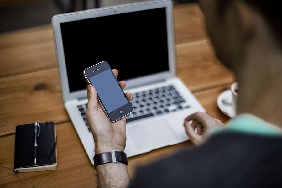 Illustrative photograph of a person holding a phone beside a laptop, not an operator account screen