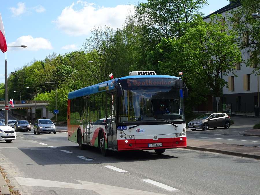 Red and white MZK Puławy bus driving along a street with flags