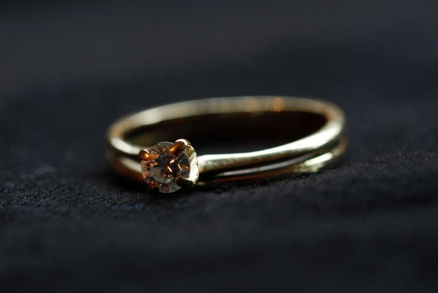 A gold engagement ring on dark fabric