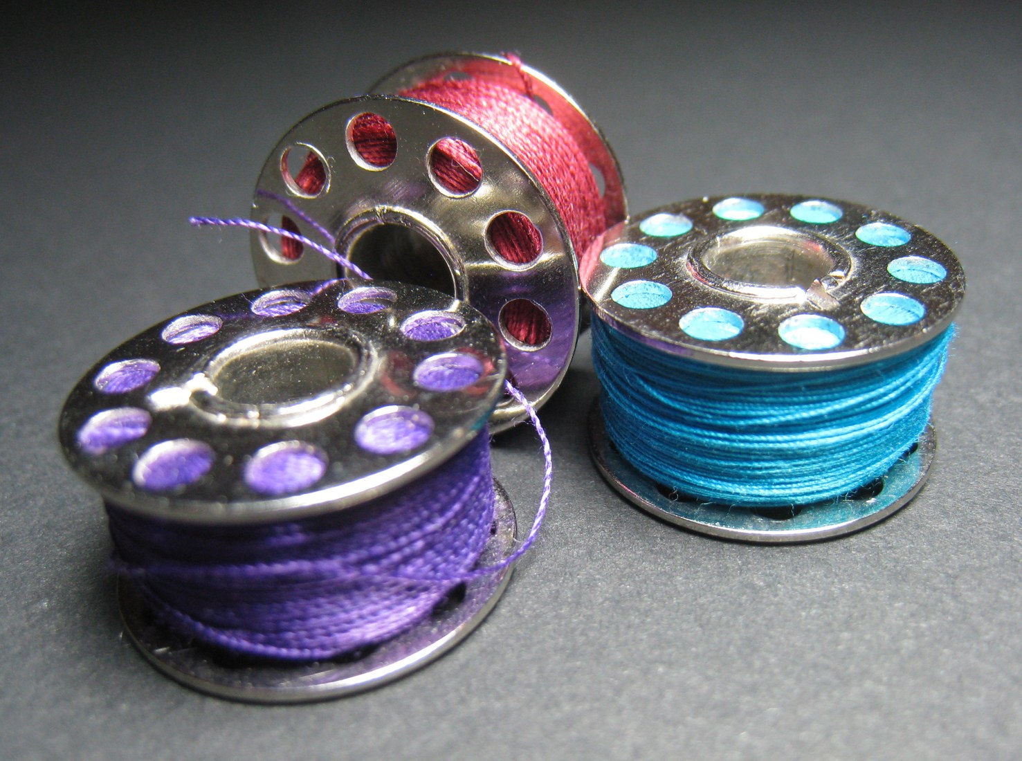 Three sewing-machine bobbins wound with coloured thread