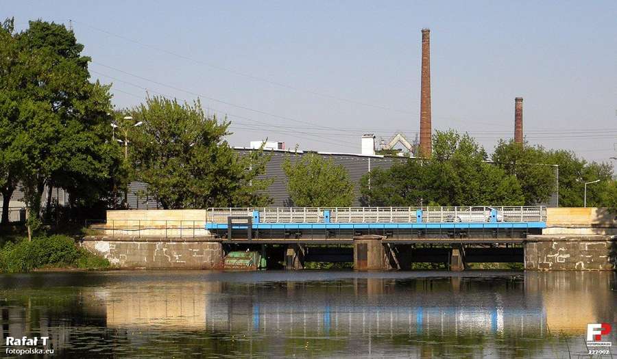 Road bridge and weir over a river in Starachowice with factory chimneys behind
