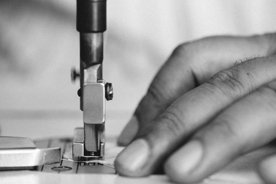 Close-up of a tailor guiding fabric under a sewing machine needle, illustrative tailoring photograph