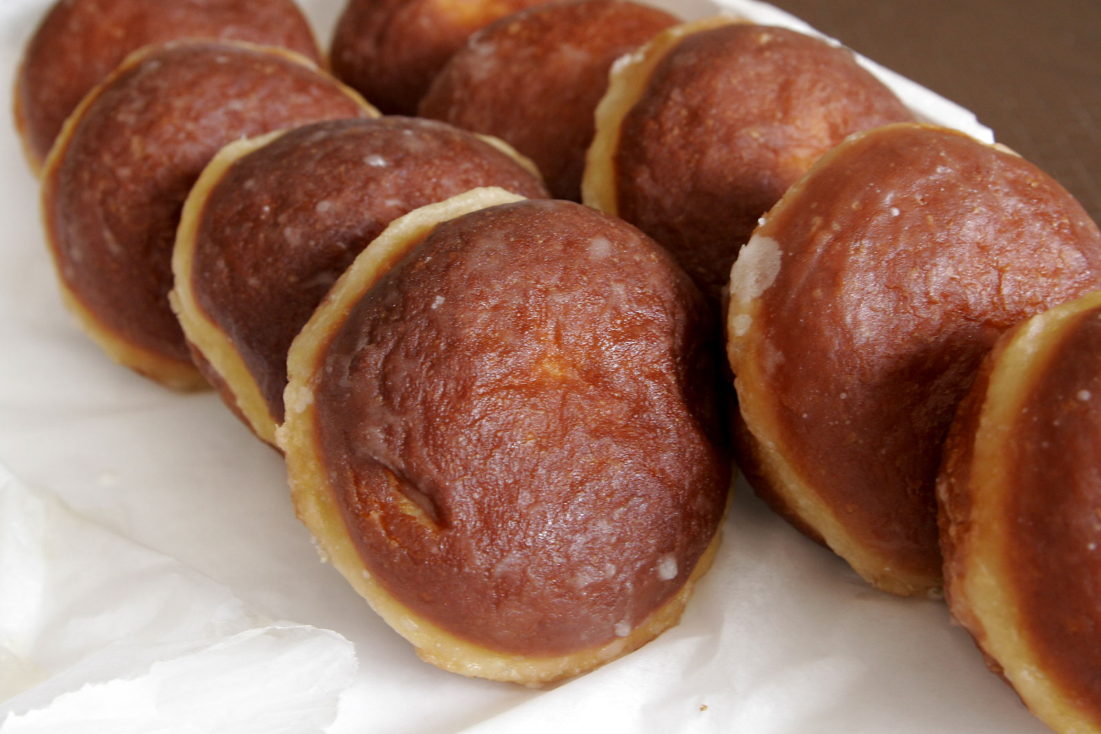 A row of freshly fried Polish pączki doughnuts lined up on white paper