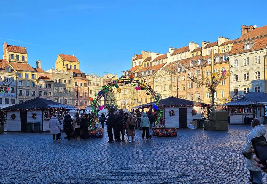 Christmas market stalls and a decorated arch on Warsaw's Old Town Market Square in December 2025