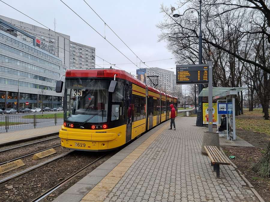 A red and yellow Warsaw tram at a stop