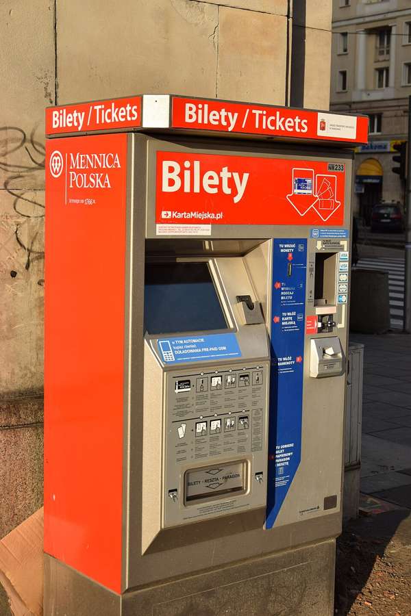 A red ZTM Warsaw public transport ticket machine displaying Bilety and Tickets on a city street