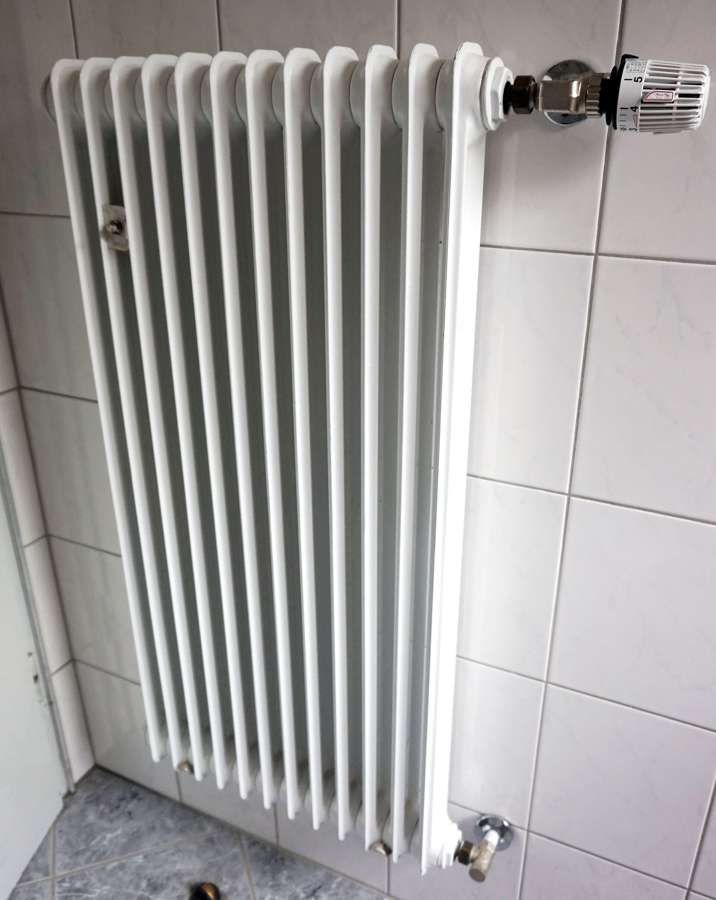 A white domestic radiator on a tiled wall - district heating carries most Warsaw homes