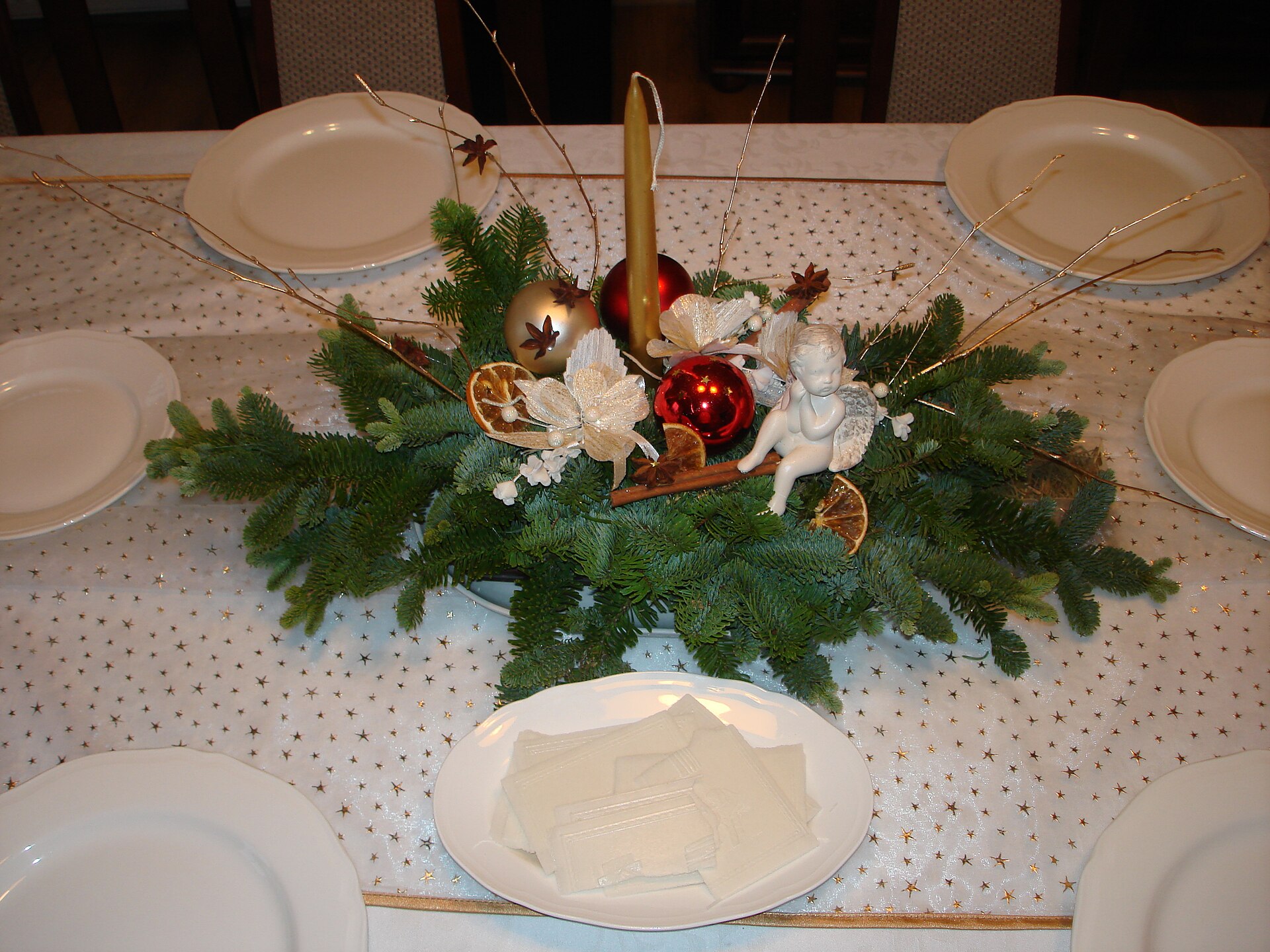 A Christmas table centrepiece of fir branches, baubles and an angel figure set for dinner