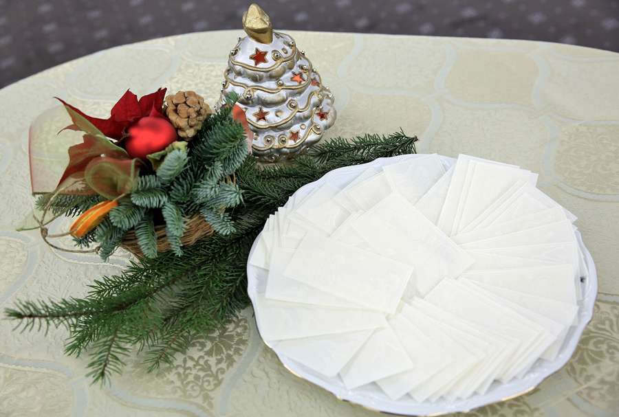 White opłatek Christmas wafers arranged on a plate beside festive greenery and a ceramic Christmas tree