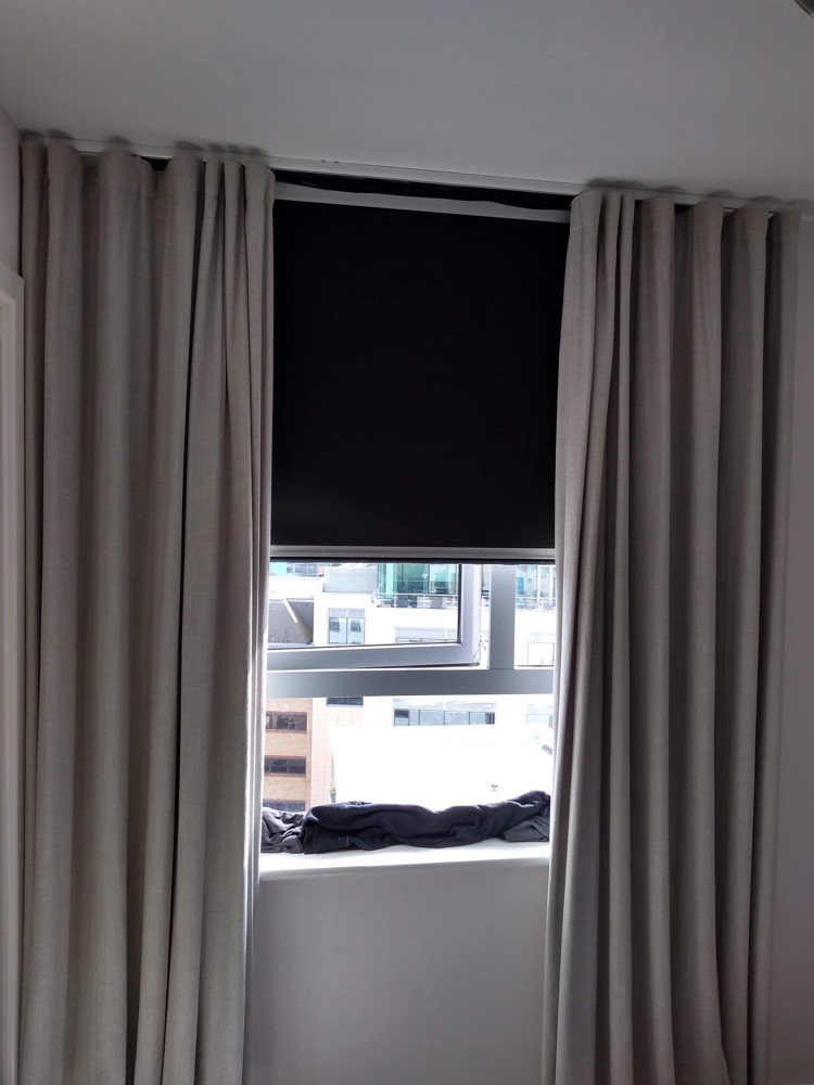 Illustrative cassette roller blind partly closed beside curtains, photographed in July 2019