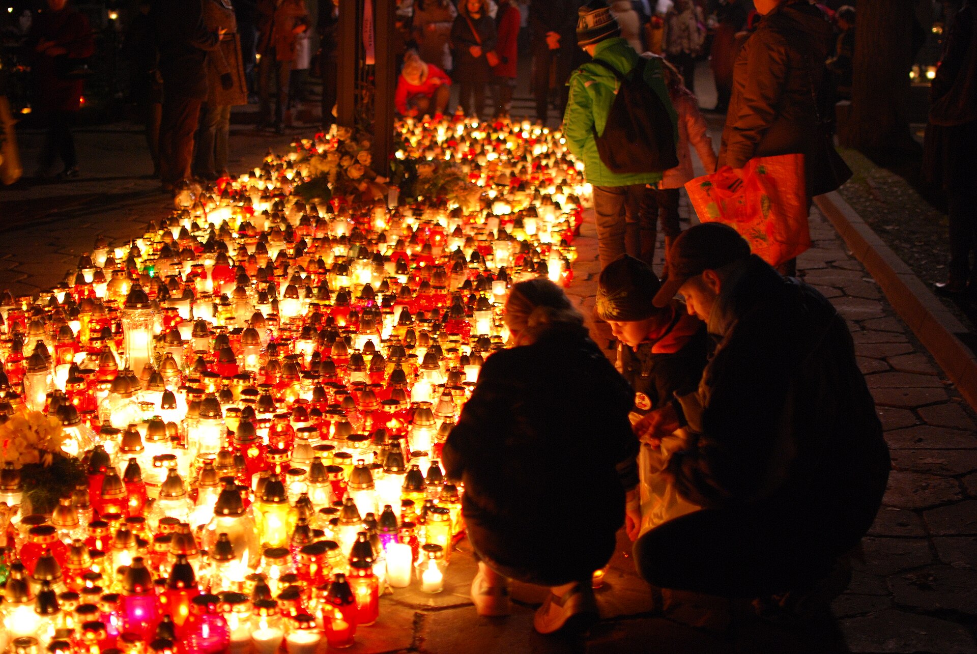 A family lighting candles among hundreds of glowing znicz lanterns on All Saints' Day in Lodz in 2014