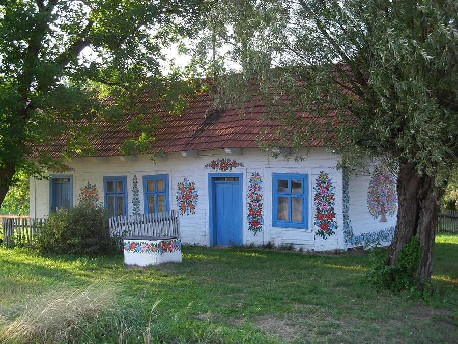 A white cottage in Zalipie with blue doors and windows, its walls covered in hand-painted floral bouquets