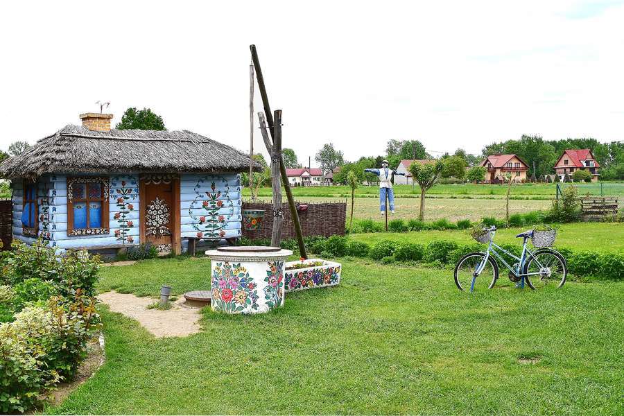 A thatched blue cottage in Zalipie with floral wall paintings and a painted well in the garden